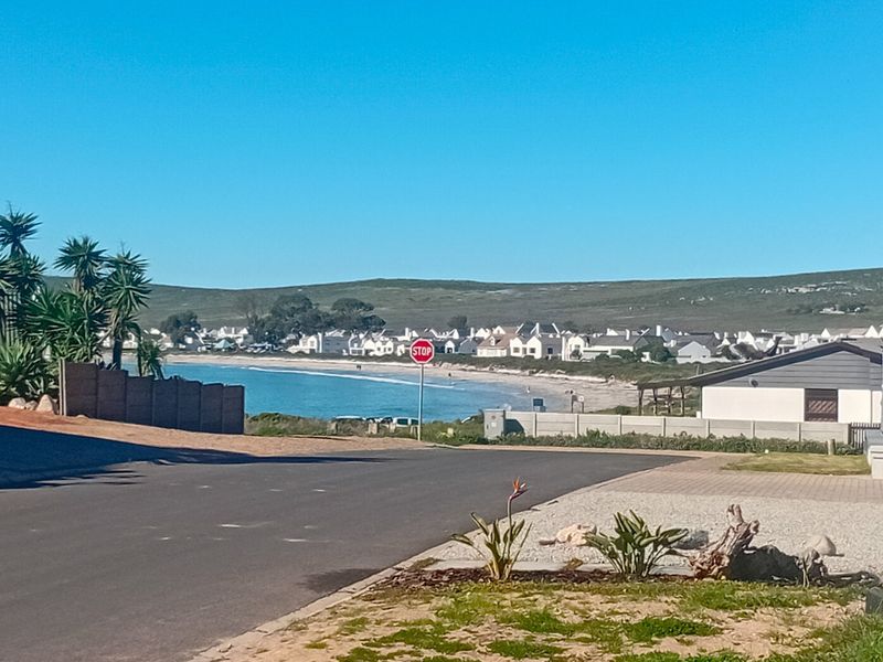 A street view looking towards the coastline, featuring paved road infrastructure and surrounding residential development in a coastal setting.