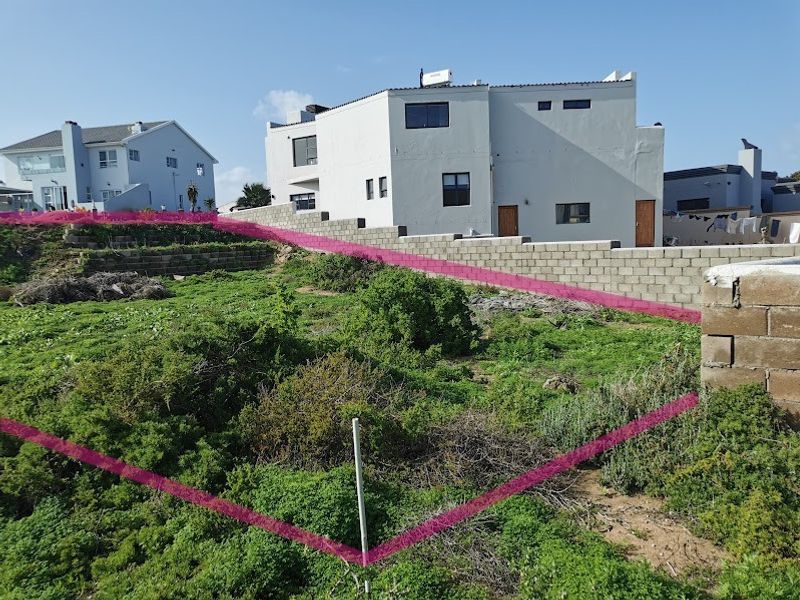 Vacant residential land plot featuring natural vegetation, boundary walls, and retaining structures, situated in a developed neighborhood.