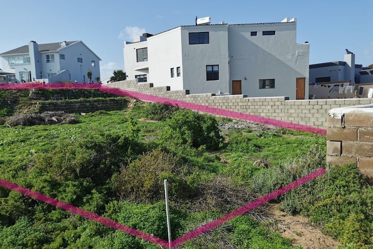 Vacant residential land plot featuring natural vegetation, boundary walls, and retaining structures, situated in a developed neighborhood.