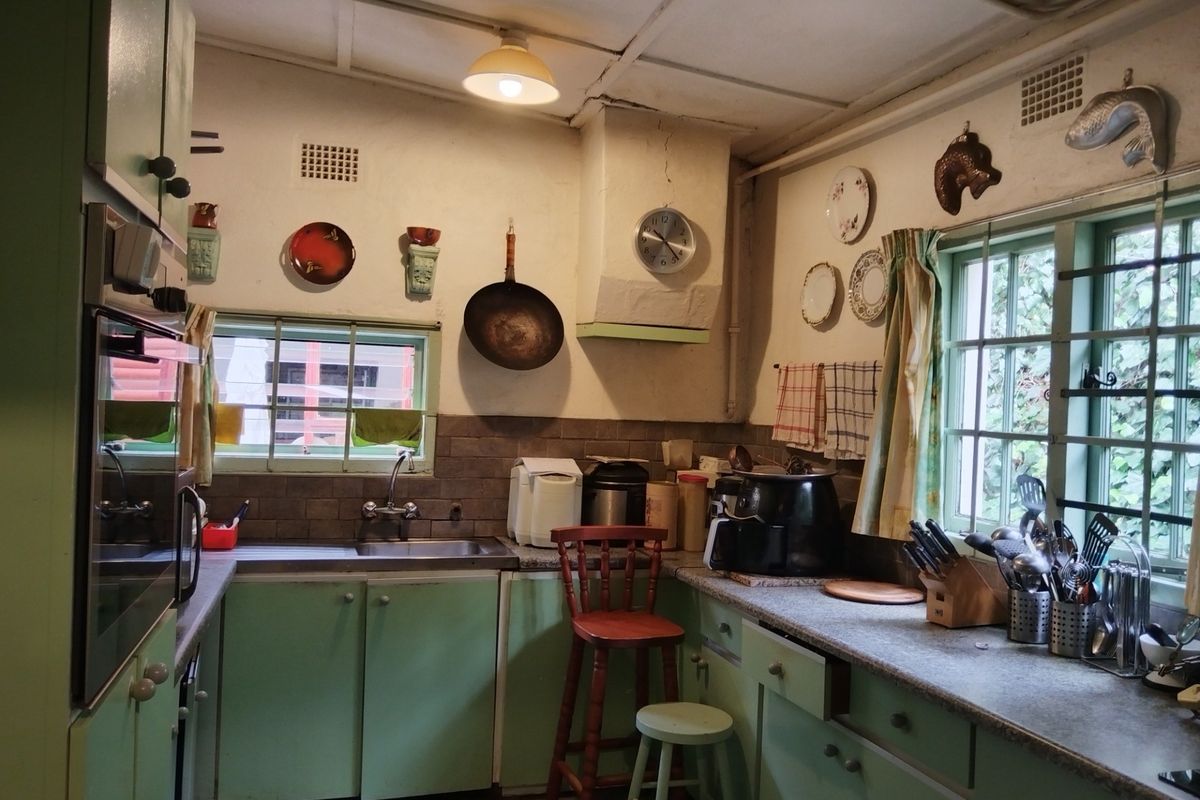 A dated kitchen featuring original green cabinetry, a built-in oven, tiled splashback, and dual windows providing natural light.