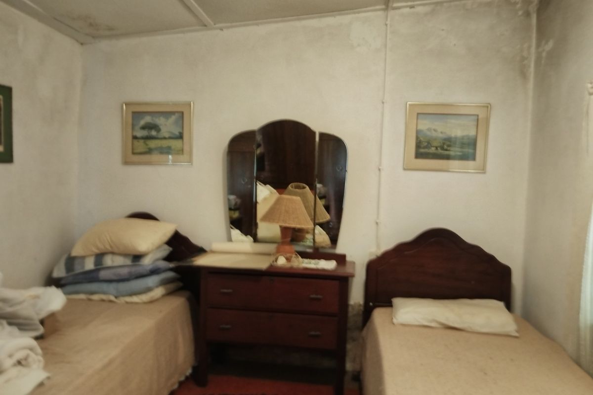 A bedroom featuring twin beds and a central vanity, showing significant signs of wear including ceiling water damage and deteriorating wall finishes.