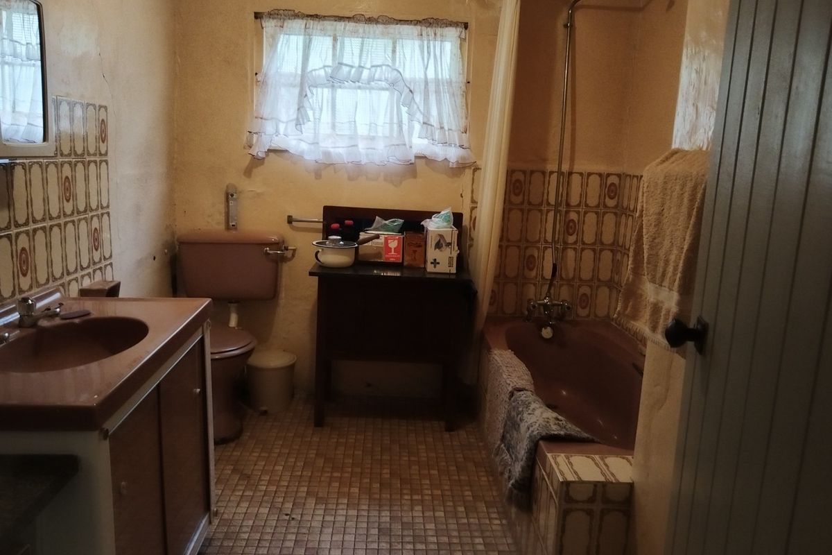 A dated bathroom featuring original colored sanitary ware, tiled splashbacks, and a shower-over-bath configuration, requiring modernization and cosmetic updates.