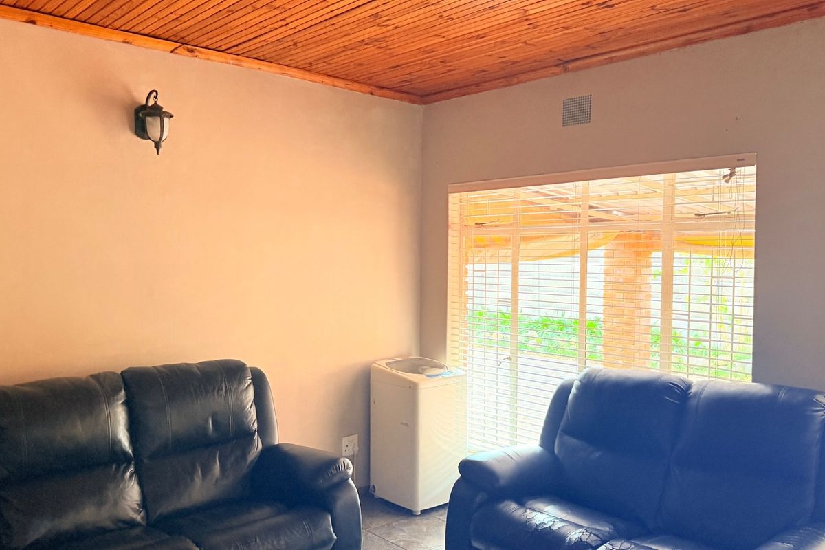 A living room featuring a wooden tongue-and-groove ceiling, tiled flooring, and large windows with fitted blinds allowing natural light.