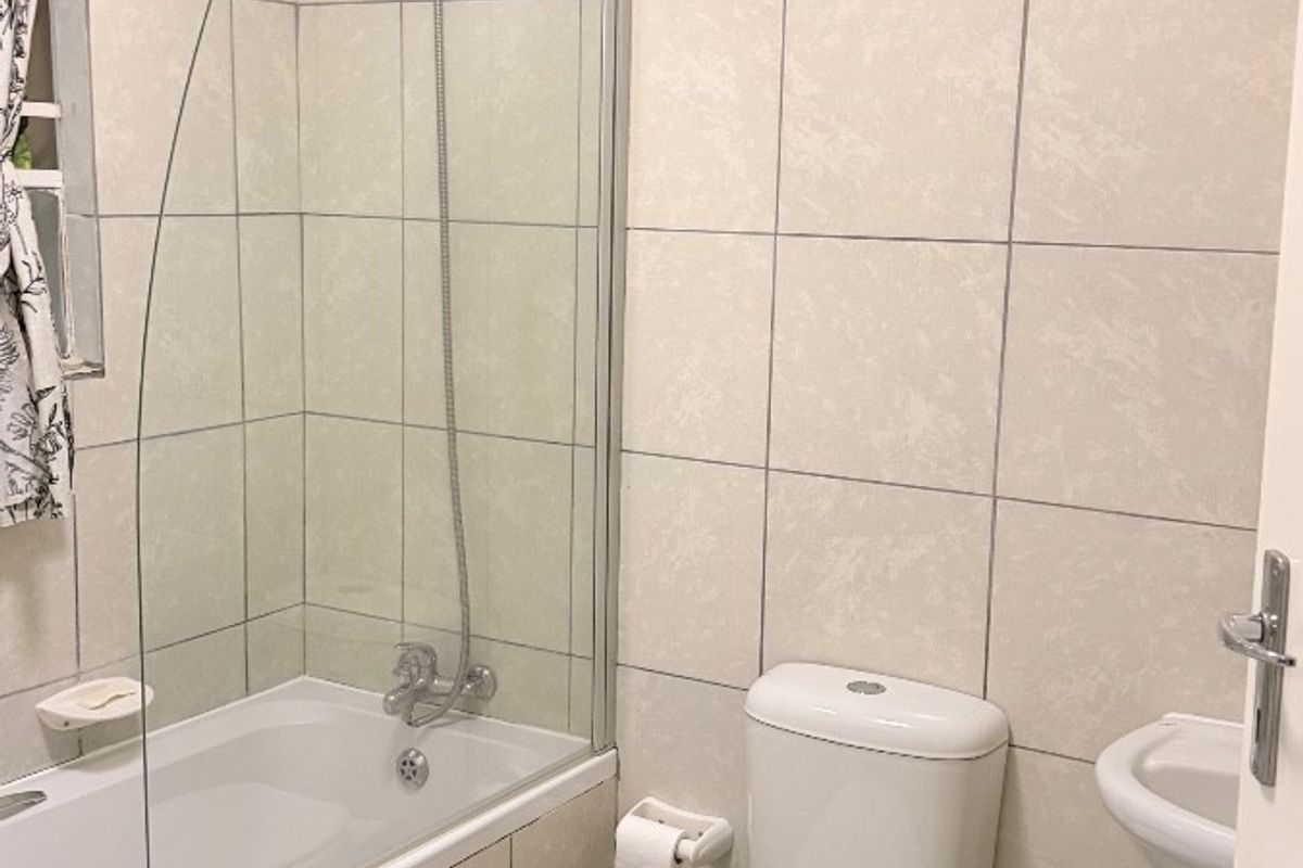 A functional bathroom featuring a bathtub with a glass shower screen, a standard toilet, and a wall-mounted basin with tiled walls and flooring.