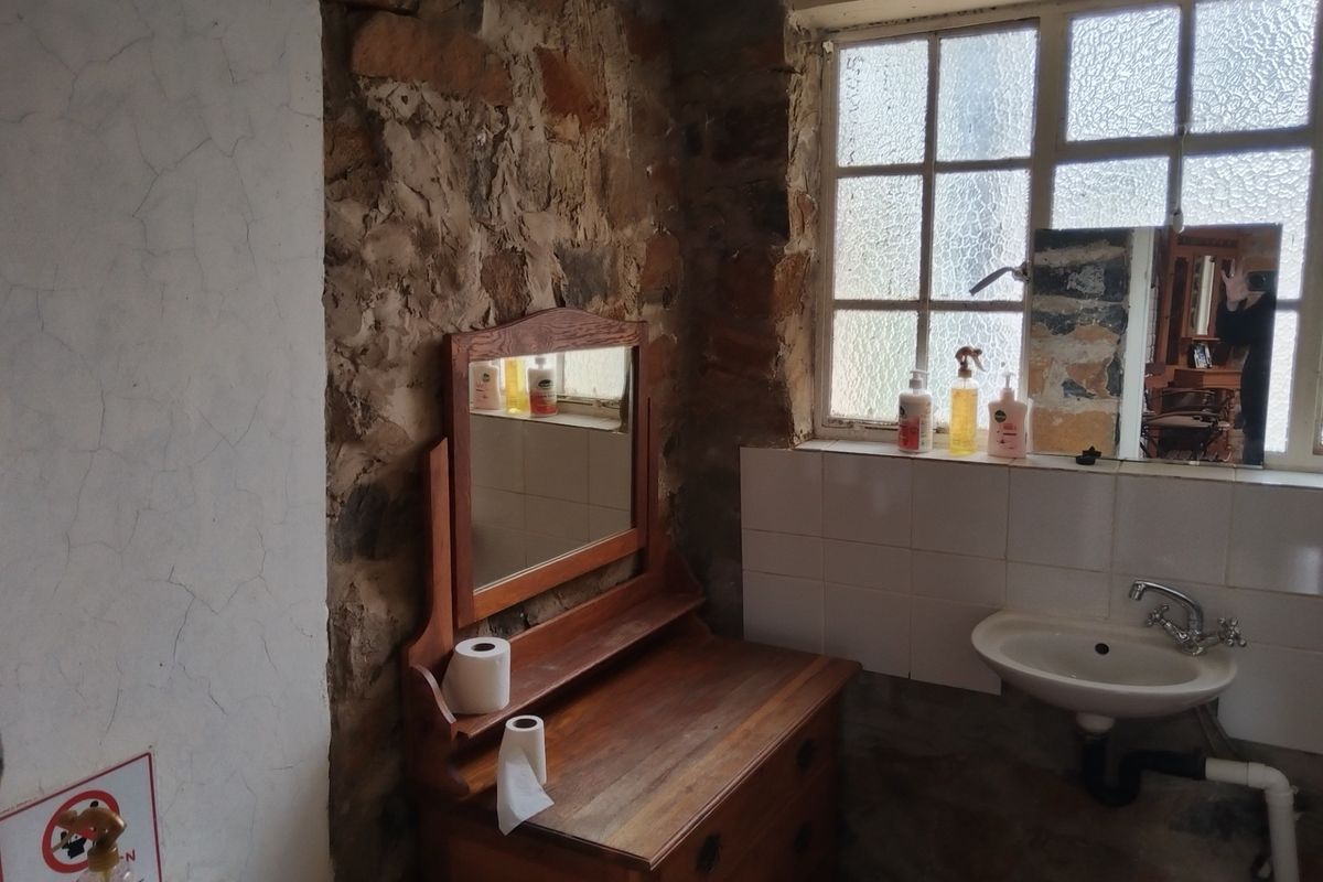 A rustic bathroom featuring exposed stone walls, a wall-mounted basin, and a multi-pane window with textured glass.