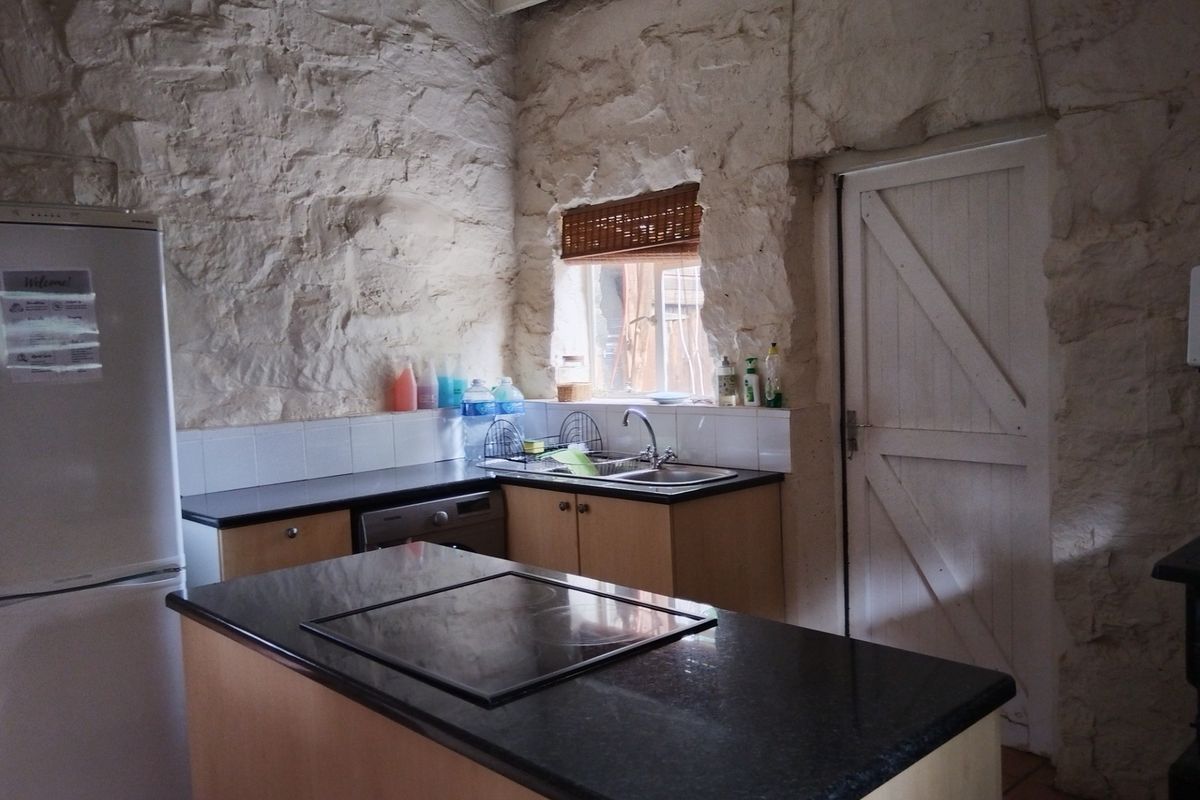 Rustic kitchen featuring exposed stone walls, a central island with a built-in cooktop, dark countertops, and a classic timber door.