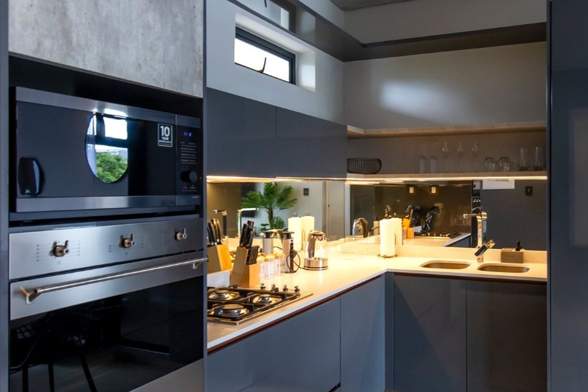 Modern kitchen featuring high-gloss cabinetry, integrated appliances including a gas hob and oven, mirrored splashback, and sleek tiled flooring.