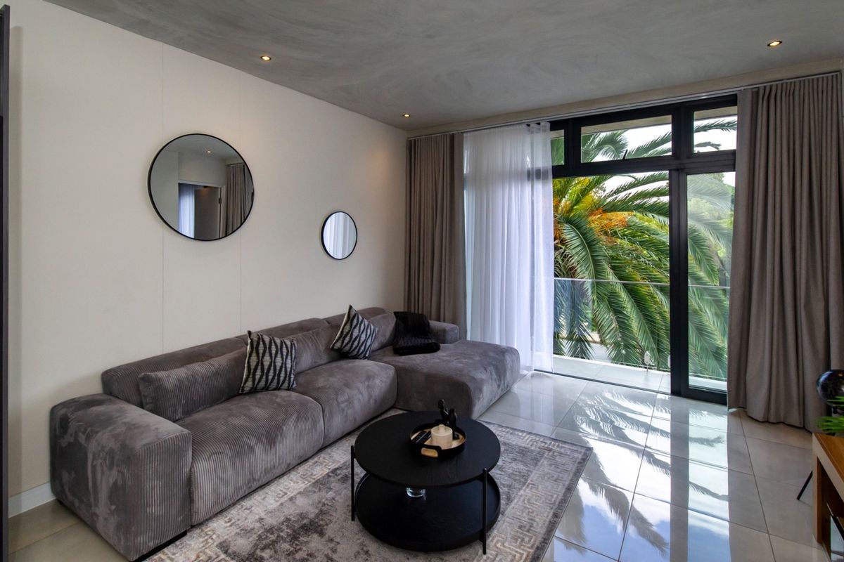Modern living room featuring polished tiled floors, recessed lighting, and a large sliding glass door opening onto a balcony with lush greenery views.