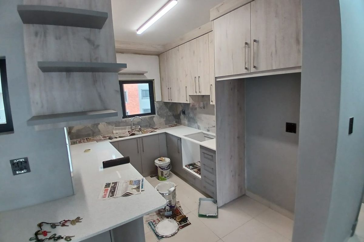 A modern kitchen under construction featuring light wood-grain cabinetry, quartz countertops, and tiled flooring, currently awaiting final appliance installation and finishing touches.