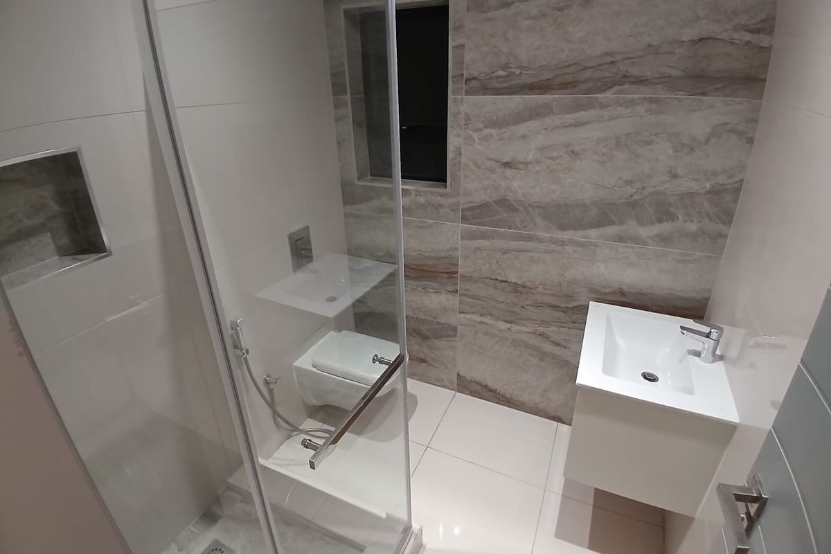 Modern bathroom featuring a glass shower enclosure, wall-mounted toilet, and a sleek vanity basin with contemporary porcelain tiling throughout.