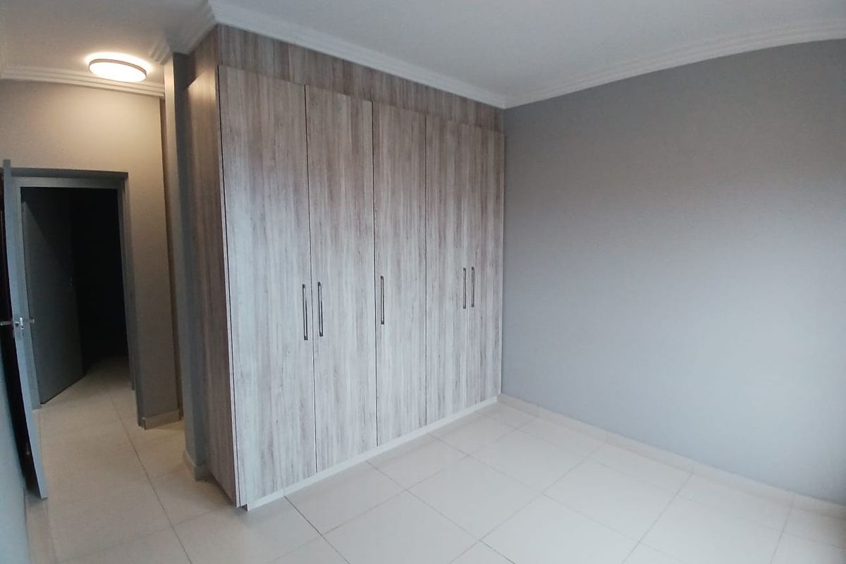 A clean, empty bedroom featuring neutral grey walls, light-toned tiled flooring, and modern wood-finish built-in cupboards.