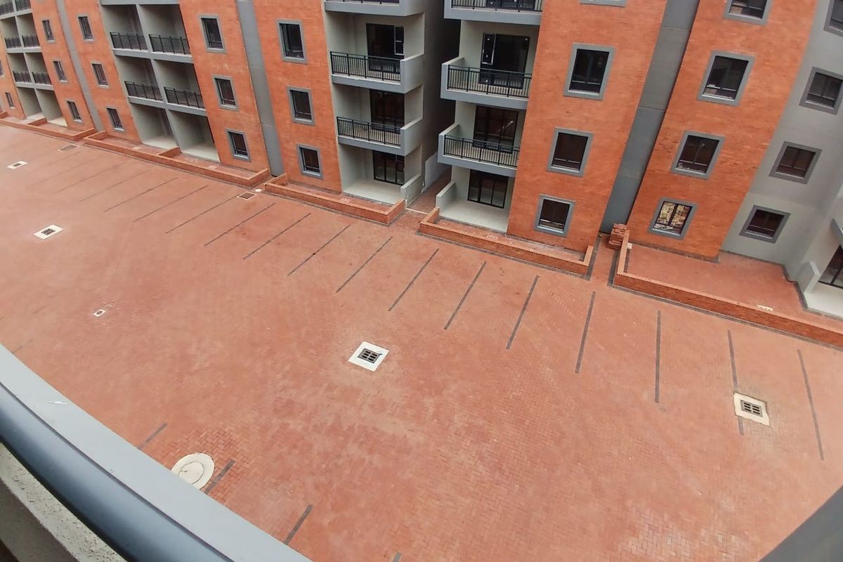 An elevated view of the apartment complex exterior, featuring a paved parking area and multiple balconies with brick facade detailing.