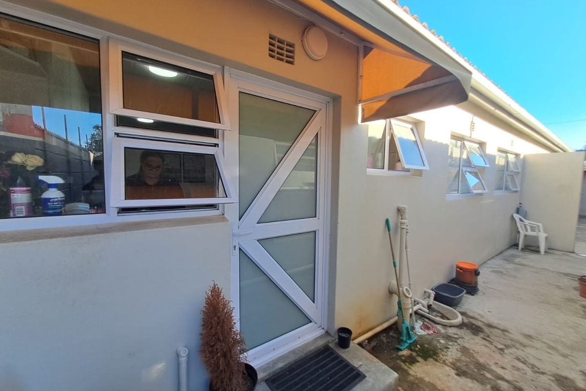 Exterior view of the rear building facade featuring white framed windows, a modern glass-panelled door, and a retractable fabric awning over the entrance.