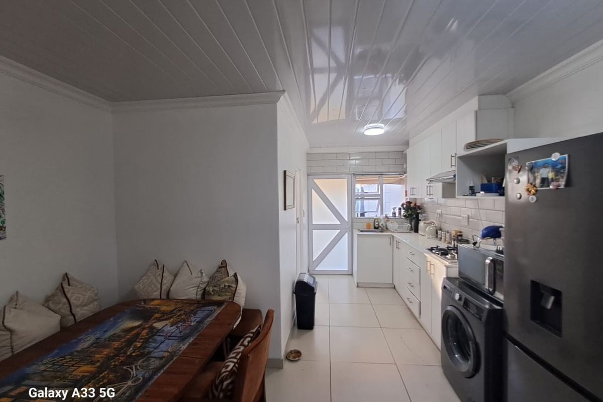 A functional kitchen featuring white cabinetry, tiled flooring, and a compact dining area, leading to an exterior door.