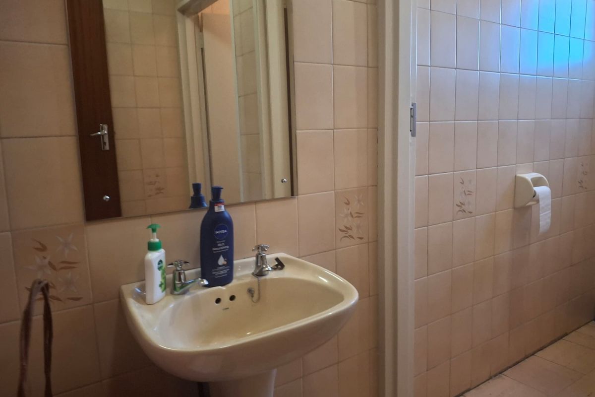 A dated bathroom featuring a pedestal basin, wall-mounted mirror, and full-height ceramic wall tiling.