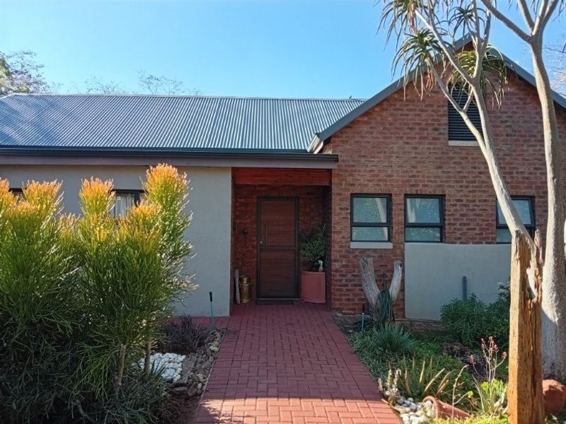 Front elevation of a retirement village unit featuring a brick and plaster facade, corrugated metal roof, and a paved entrance path.