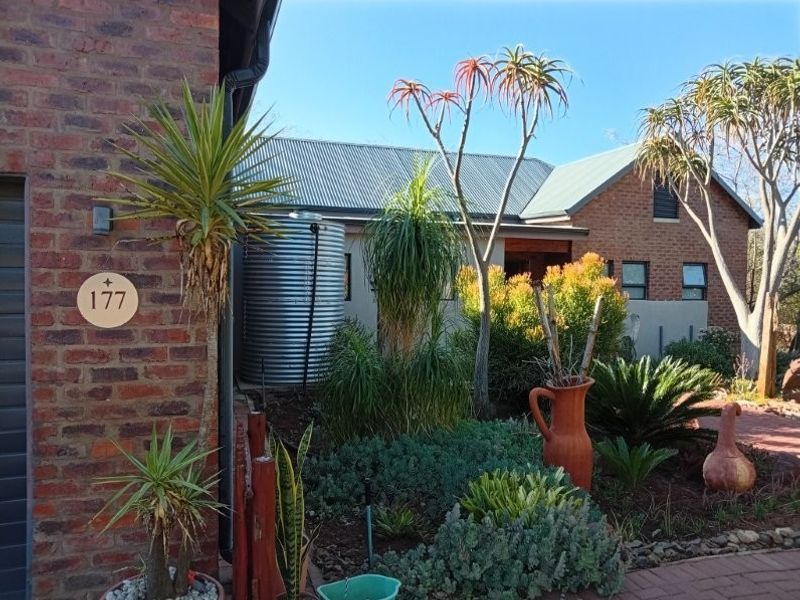 Front elevation of a retirement village unit featuring face brick construction, a corrugated metal roof, and a landscaped garden with a rainwater tank.