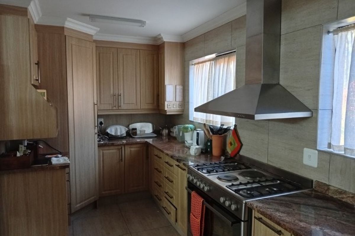 A functional kitchen featuring wooden cabinetry, granite countertops, a stainless steel extractor fan, and a gas hob with an integrated oven.