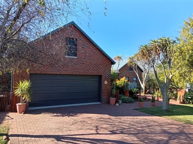 Front view of a brick retirement village residence featuring a double garage, paved driveway, and established garden surroundings.