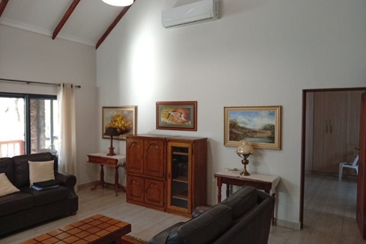 Spacious living room featuring a high vaulted ceiling with exposed timber beams, tiled flooring, and a wall-mounted split-system air conditioner.