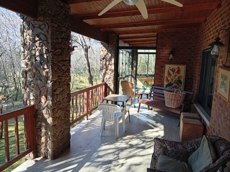 A covered patio featuring stone-clad pillars, exposed timber ceiling with a fan, and brick walls, offering a pleasant outdoor living space.