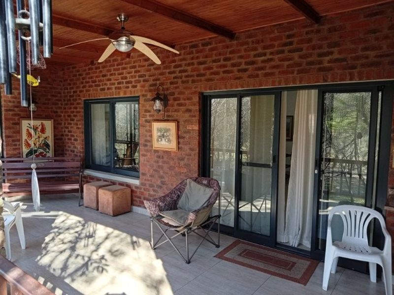 A covered patio featuring exposed brick walls, a timber ceiling with a ceiling fan, and large sliding glass doors leading into the home.