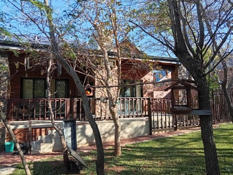Rear view of a retirement village unit featuring stone and brick exterior, a raised timber deck, and sliding glass doors leading to a garden area.
