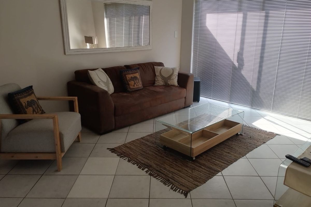 A bright living room featuring neutral floor tiles and large sliding glass doors with fitted venetian blinds, providing ample natural light.