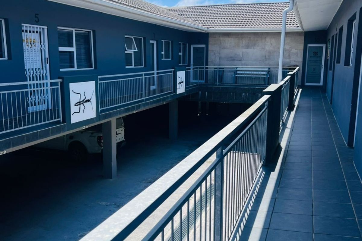 An exterior view of an office building featuring a tiled walkway, metal railings, and a covered parking area below.