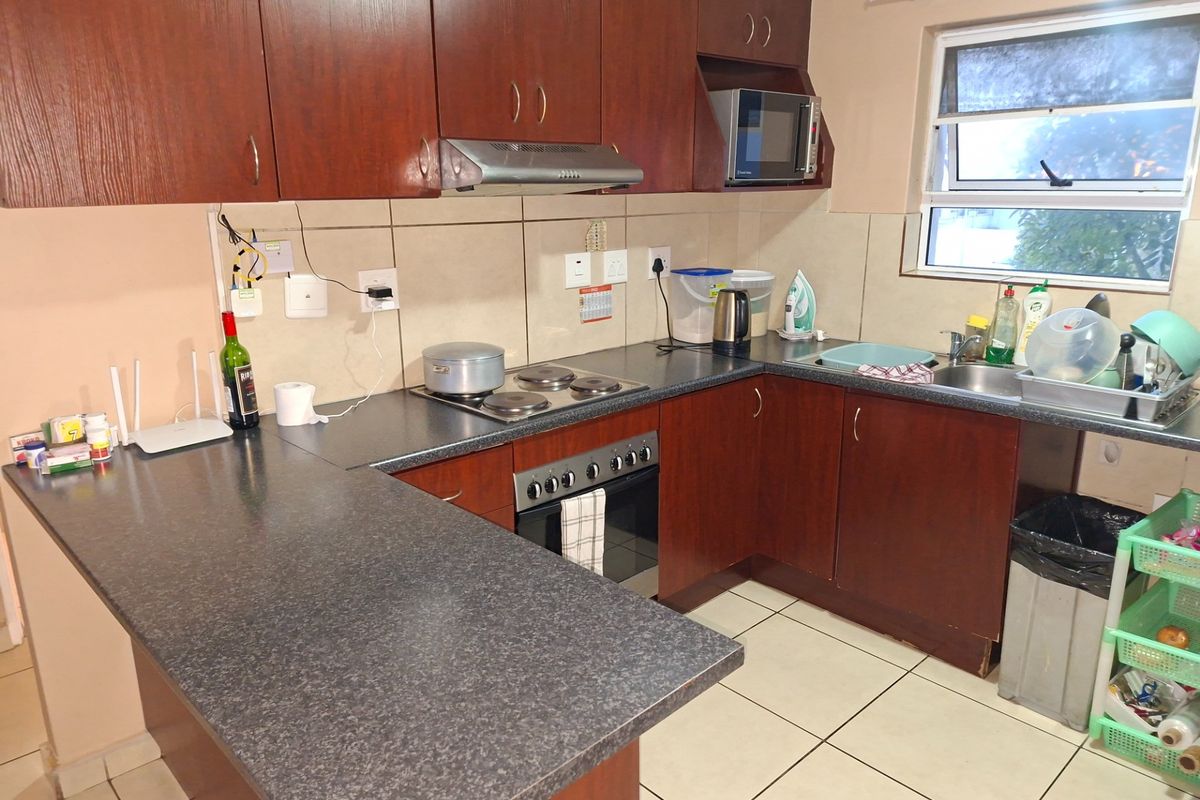 A functional kitchen featuring dark wood-look cabinetry, laminate countertops, built-in oven and hob, and tiled flooring with a practical layout.