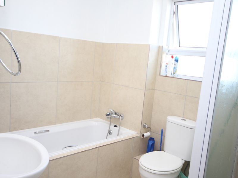 A functional bathroom featuring a bathtub, toilet, basin, and tiled walls with a window for natural light.