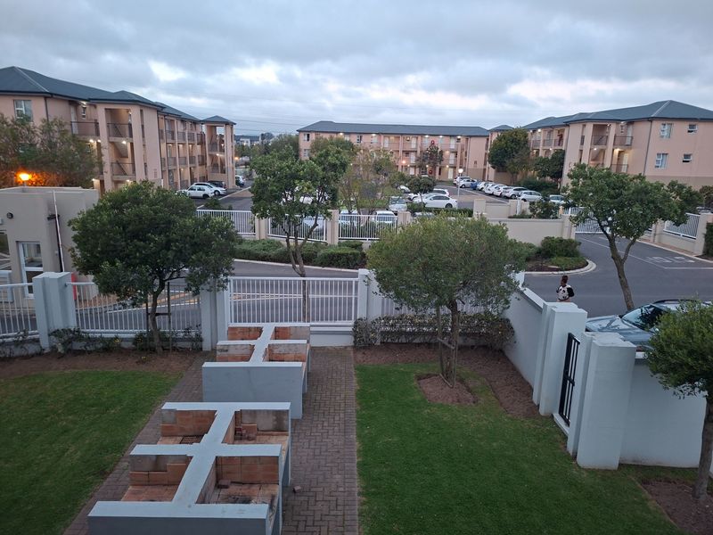 Communal outdoor area featuring built-in braai facilities, paved patio space, and landscaped garden within a secure apartment complex.