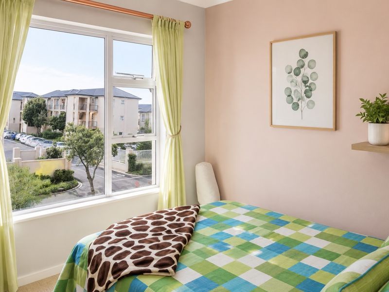 A bright bedroom featuring a large window with natural light and views of the surrounding apartment complex.