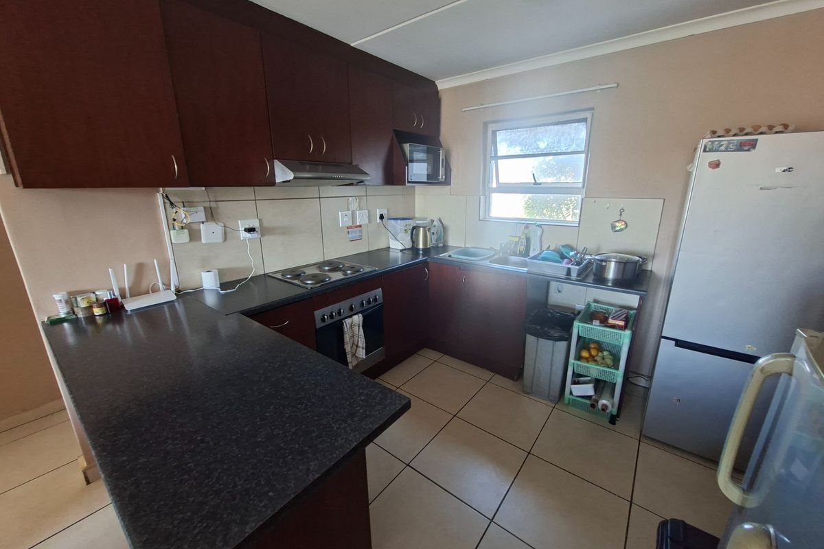 A functional kitchen featuring dark wood cabinetry, laminate countertops, an electric hob, built-in oven, and tiled flooring with a window for natural light.