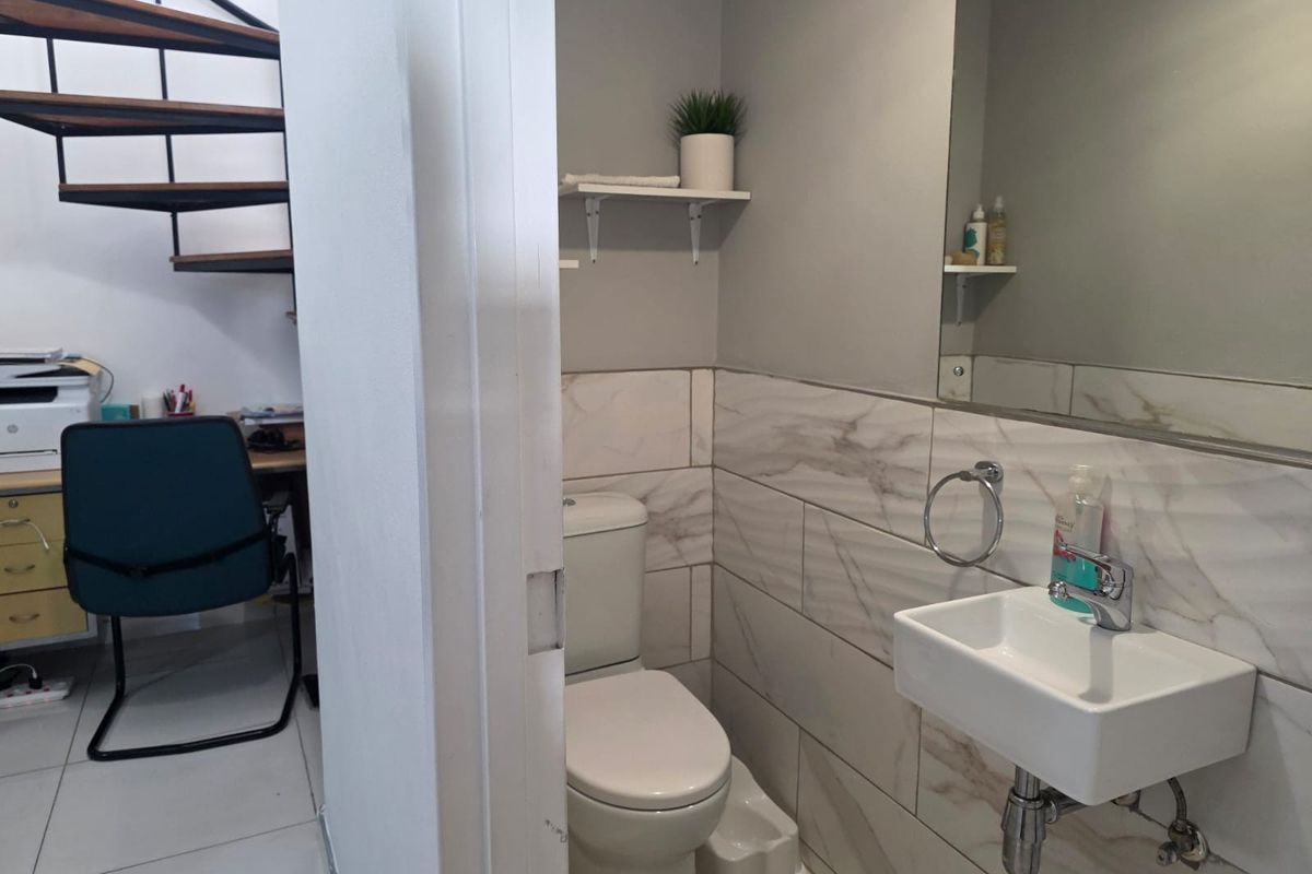 A compact guest bathroom featuring modern marble-look wall tiles, a wall-mounted basin, and a toilet, situated adjacent to a home office area.