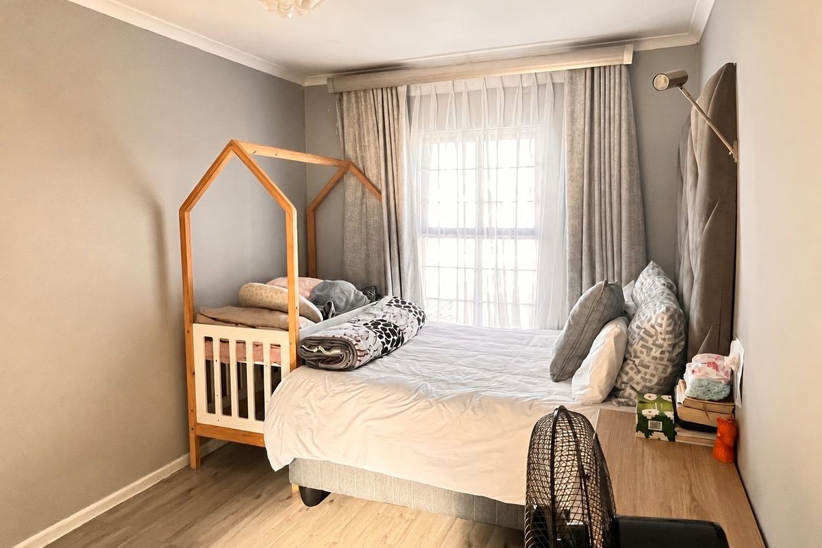 A well-maintained bedroom featuring neutral wall tones, laminate flooring, and a built-in headboard with integrated lighting.
