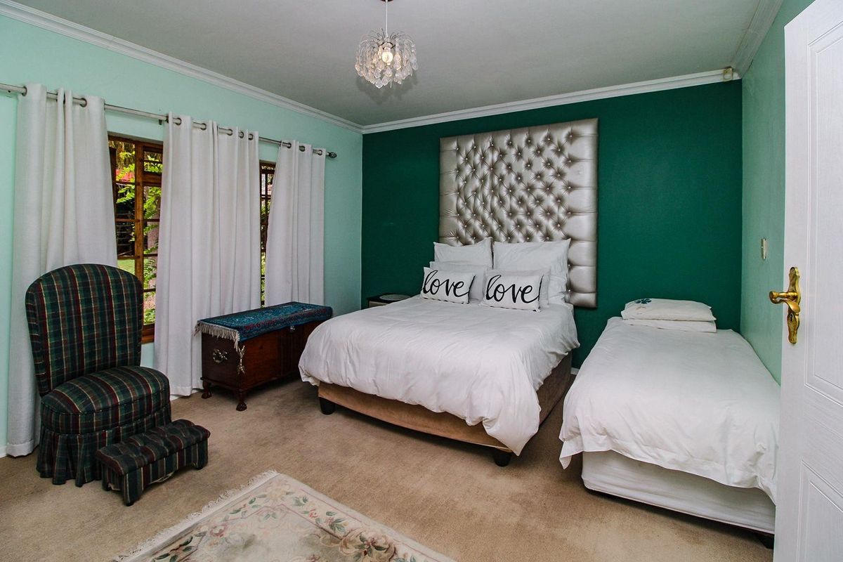 A spacious bedroom featuring a prominent green accent wall, neutral carpeting, and large windows allowing for natural light.