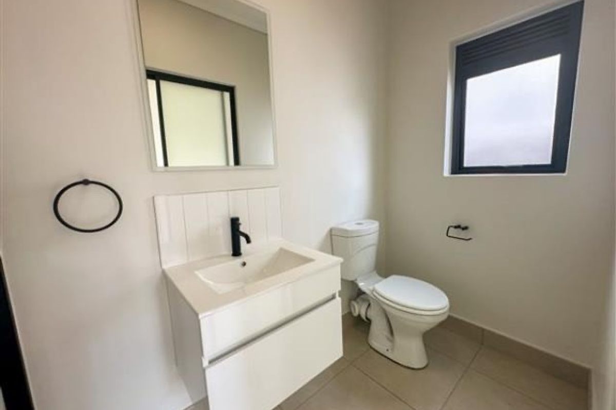 A modern, minimalist guest bathroom featuring a wall-mounted vanity with a basin, a sleek black faucet, and a contemporary toilet.