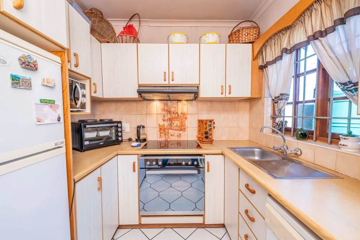 A functional kitchen featuring laminate countertops, built-in cabinetry, an electric hob with extractor fan, and a stainless steel double sink.
