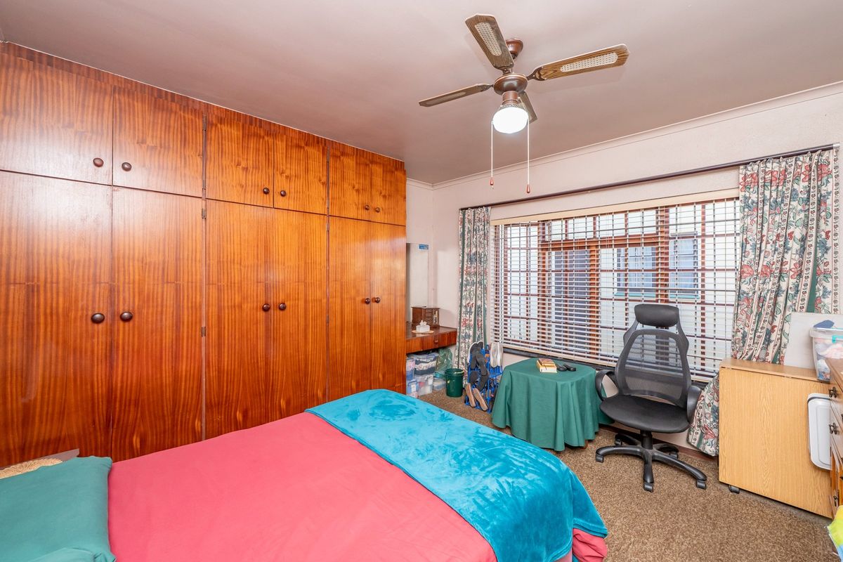 A bedroom featuring extensive built-in wooden cabinetry, a ceiling fan, and a window fitted with security bars.