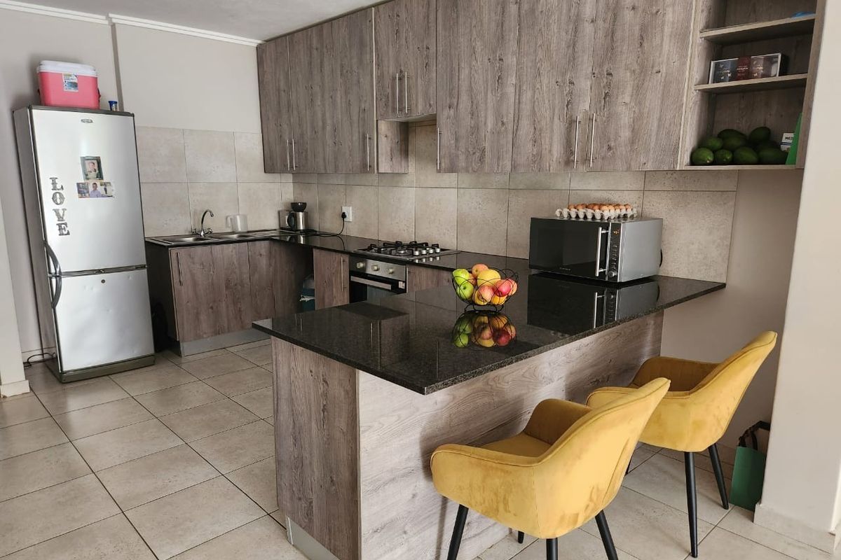 Modern kitchen featuring wood-grain cabinetry, granite countertops, a breakfast bar, and built-in gas hob with oven.