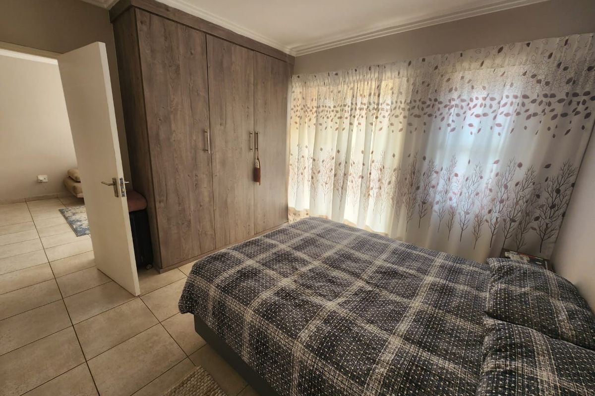 A well-maintained bedroom featuring built-in wooden cabinetry, tiled flooring, and large windows with curtains, offering a clean and functional living space.