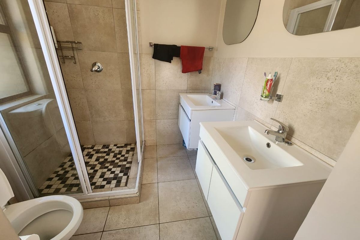 A functional bathroom featuring a glass-enclosed shower, dual vanity units with modern basins, and neutral floor-to-ceiling wall tiling.