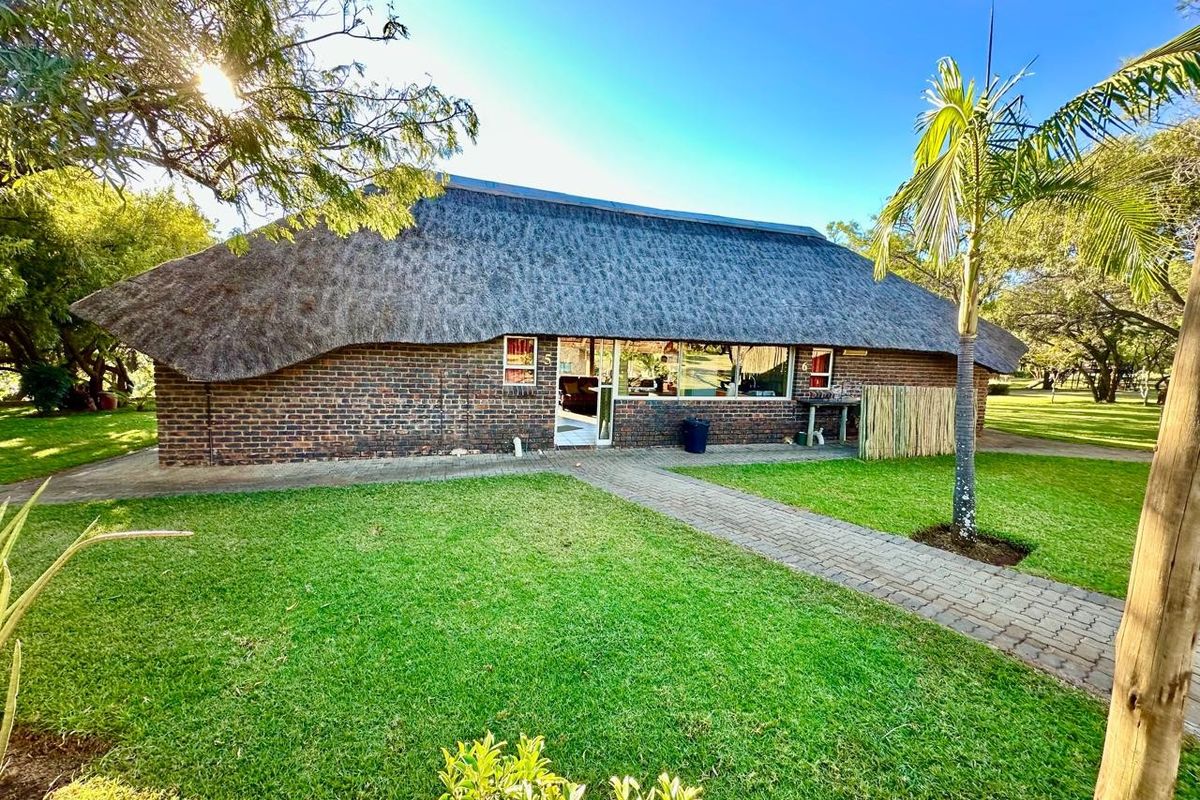 A rear view of a farm-style building featuring a traditional thatch roof, face brick exterior, and a well-maintained lawn with a paved walkway.