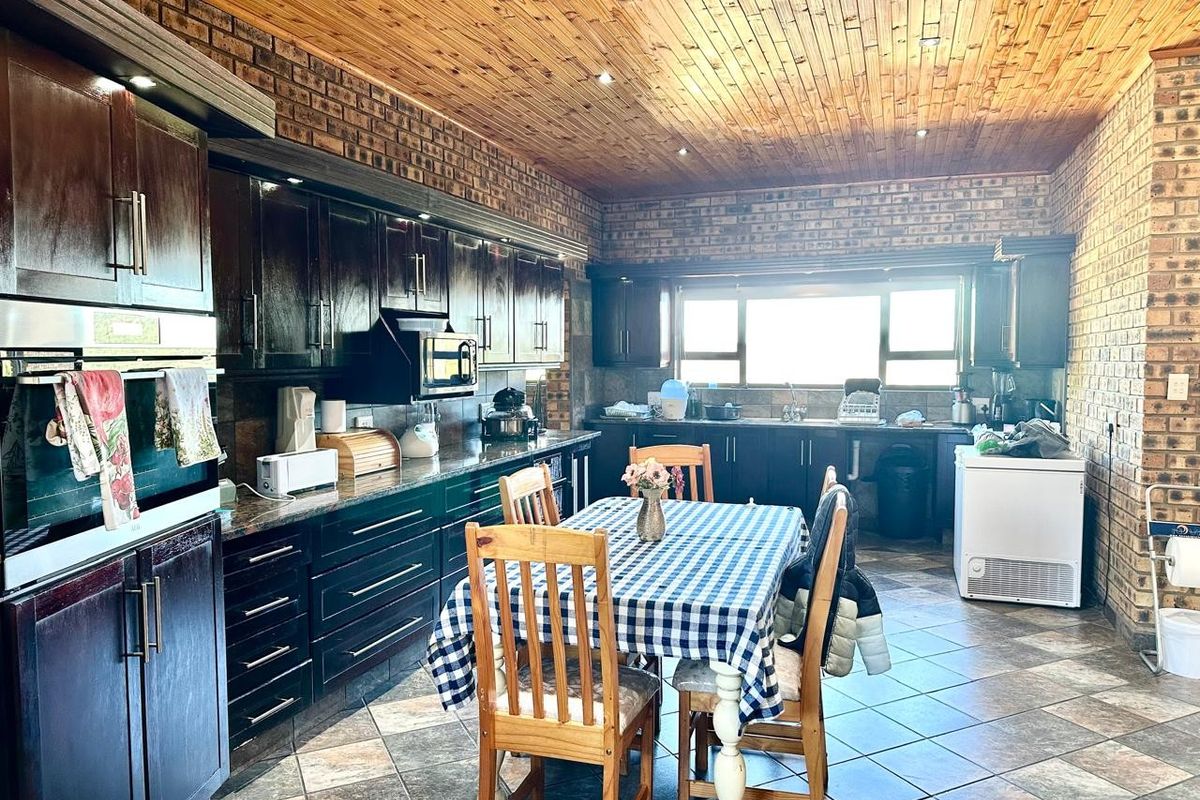 Spacious farmhouse kitchen featuring dark wood cabinetry, granite countertops, exposed brick walls, and a warm timber ceiling with recessed lighting.