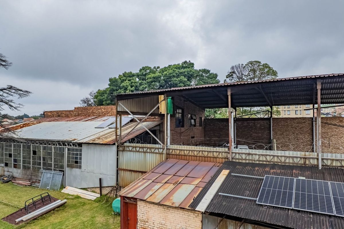 Aerial view of industrial-style outbuildings on a small holding, featuring corrugated metal roofing, brick structures, and installed solar panels.