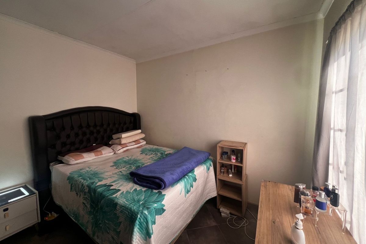 A standard bedroom featuring tiled flooring and a window with curtaining, providing a functional sleeping space.
