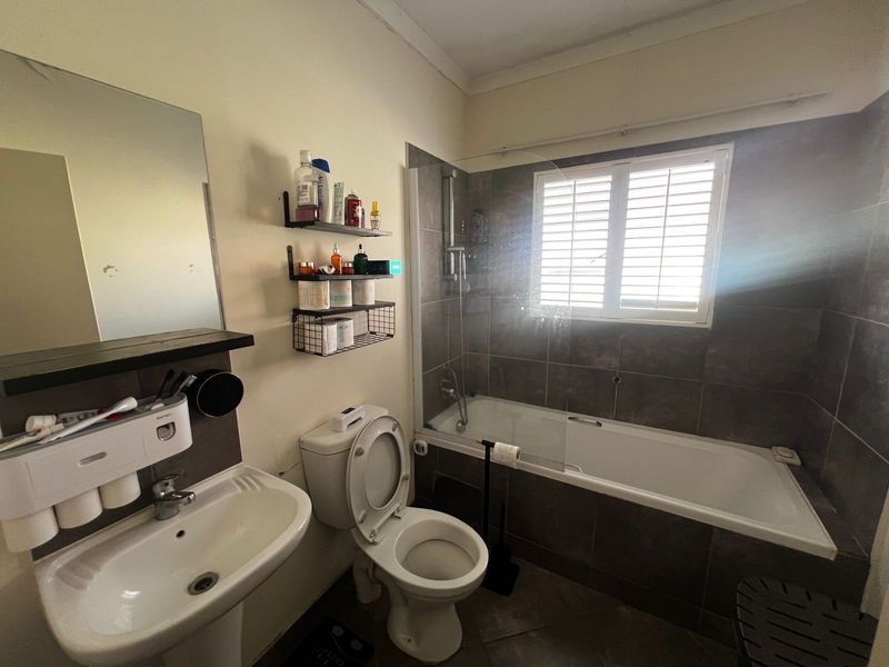 A functional bathroom featuring a pedestal sink, a toilet, and a bathtub with a glass shower screen and tiled surround.