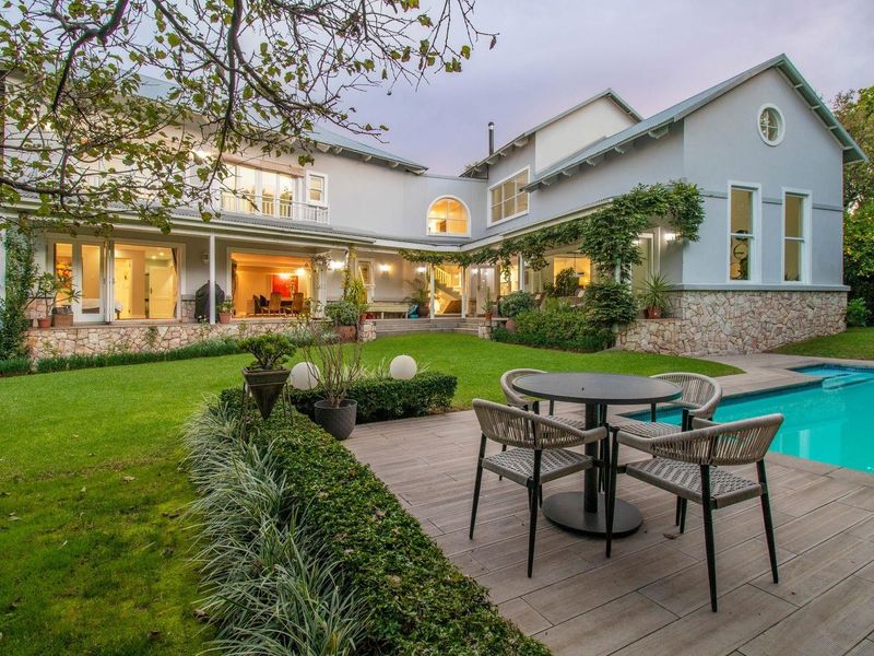Spacious rear exterior featuring a well-maintained garden, swimming pool, timber decking, and a covered patio area attached to the main residence.