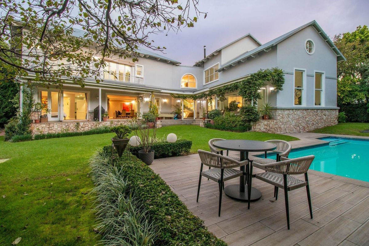 Spacious rear exterior featuring a well-maintained garden, swimming pool, timber decking, and a covered patio area attached to the main residence.